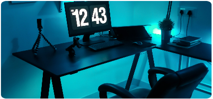 A personal workplace with a monitor displaying the time 12:43
