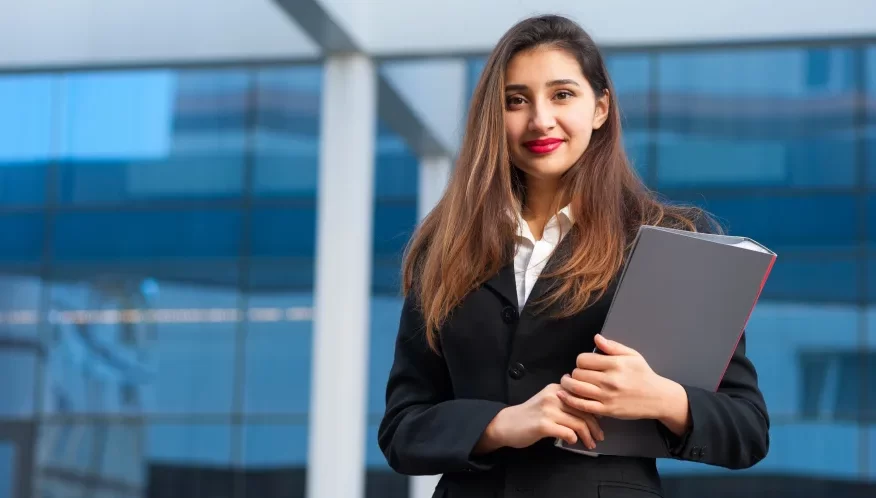 A businesswoman holding a folder in front of a building.
