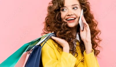 A girl with curly hair holding multiple shopping bags in her one hand and talking on phone with the other hand