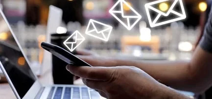 A person working on a laptop and mobile while email icons fly by