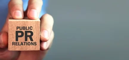 A person holding a wooden block with Public Relations (PR) printed on it