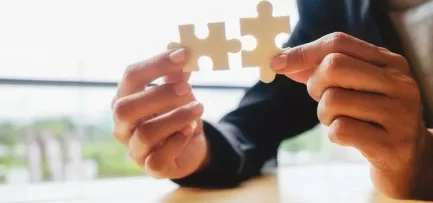 Two hands of a person trying to join two pieces of a jigsaw puzzle