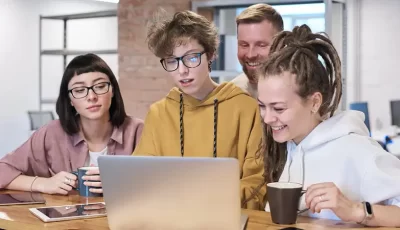 Four people gathered at a desk and looking at the laptop screen