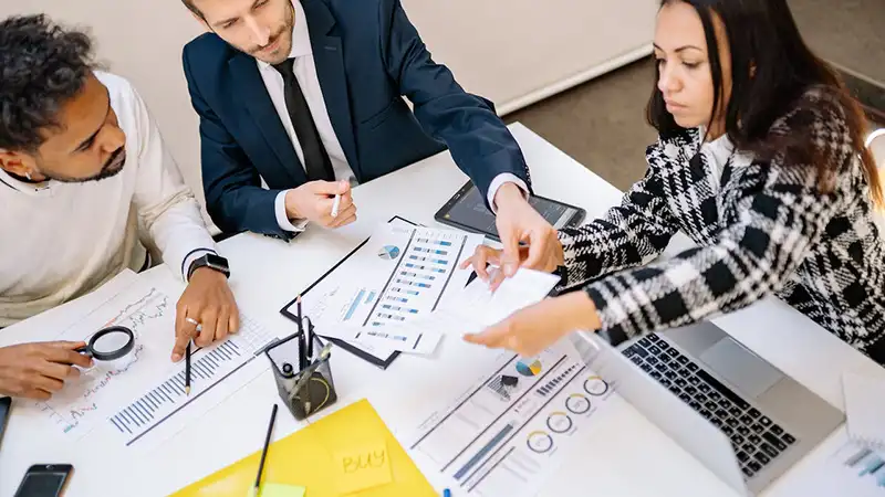 Three people sitting around a table and working together with office stationary on the table