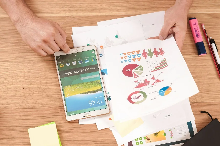 A person pointing at a tablet with different reports placed on the table