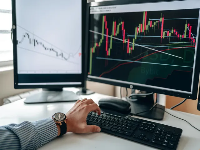 A person analyzing financial charts on two computer screens using a keyboard and mouse