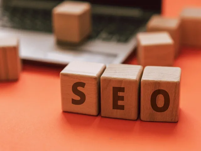 Wooden-blocks-with-the-letters-SEO-are-placed-on-an-orange-surface-in-front-of-a-laptop