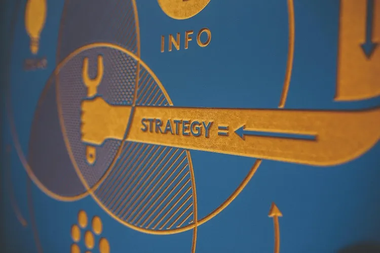A close-up of a blue and gold graphic featuring the word STRATEGY with arrows, surrounded by symbols like light bulbs and a wrench